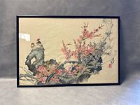 Full view of framed painting showing two birds perched on a rock with blooming pink plum blossom branches extending horizontally across the composition.