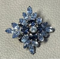 Front view of vintage brooch showing clear central crystal, surrounding blue crystals in various shapes, set in silver-tone metal.