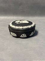 Side and top angle view of black Wedgwood jasperware trinket box showing scalloped edges and white relief decorations.