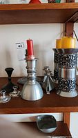 Photo showing three tall pewter candlesticks with red and yellow candles, and smaller holders at shelf level