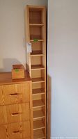 Tall wooden CD rack with adjustable shelves next to a wooden dresser.