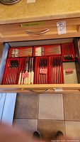 Open drawer with six red trays holding sections of cutlery (knives, forks, spoons)