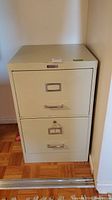 Front and slight angle view of beige two-drawer filing cabinet showing keyhole and label holders on drawers.