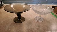 Two footed serving dishes together on countertop, amber and clear textured glass, showing general condition and size.