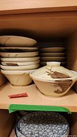 Shelf view showing stacked set of bowls, lids, and saucers with Japanese painting motif.
