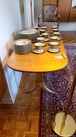 Full view of birch wood drop leaf side table with stacked dishes and cups on top, showing warm finish and two drop leaves extended.