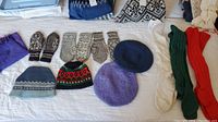 Overview of traditional Norwegian wool mittens and knitted hats plus a scarf laid flat on a bed, showing patterns and colors.