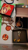 Assorted modern and MCM style costume jewelry including necklaces and pendants shown in an open box and laid out on a flat surface