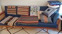 Several assorted woven mats and throw pillows arranged on a blue sofa couch showing a variety of patterns and colors.