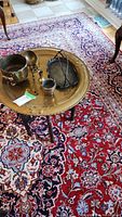 Photo showing the brass topped table with brass small pot, ladle, scissors, candle holder, and tray placed on top, all arranged on a patterned rug.
