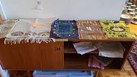 Wide view of wooden cabinet top with folded embroidered table linens including table runner and placemats.