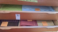 Drawers with five folded tablecloths: green, light blue, dark brown patterned, red-orange, yellow patterned