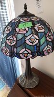 Full view of Tiffany style stained glass shade and metal base on a wood surface