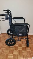 Side view of Medline Excel Deluxe aluminum folding transport chair showing frame, wheels, side pocket, and armrest.