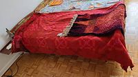 Twin bed covered by red woven blanket with geometric motifs