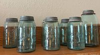 Eight antique blue glass Ball Mason jars arranged in a row on a wooden surface showing the embossed logo and zinc lids.