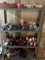 Shelves with multiple candles and candle holders in various shapes and colors including heart-shaped, glass, and ceramic pieces