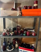 Metal shelving with assorted candles and candle holders in red, blue, and clear glass, displaying a wide variety of sizes and shapes.
