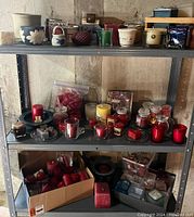 Shelf with assorted candles and candle holders including jars, pillar candles, votives, and decorative holders.