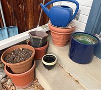 Photo of various ceramic planters and pots placed on outdoor steps with soil and a blue watering can.