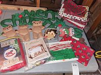Wide shot of table showing all Christmas craft items and decorations including fabric, kits, and teddy bear ornaments.