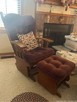 Glider chair and ottoman set shown side view with decorative pillow, against indoor setting near a fireplace.