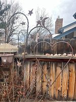 Full view of the iron heart shaped plant hanger with decorative stars and moon on curved hooks, situated outdoors against a wooden fence.