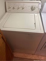 Front view of a white Kenmore top load washing machine with closed lid and control panel visible, including dials and knobs.