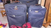 Front view of two of the suitcases standing upright showing front pockets, fabric material, zippers, and leather accents.