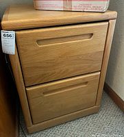 Front view of the oak filing cabinet showing the two drawers with recessed handles and natural wood grain finish.