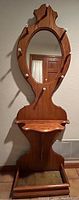 View of full oak hall tree showing oval mirror, eight white ceramic-tipped coat hooks, curved shelf, and umbrella stand base.
