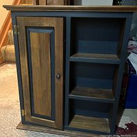 Front view of the painted wood wall cabinet showing the left door and three open shelves on the right.