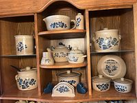 Photo of Pfaltzgraff Folk Art pieces displayed in a wooden cabinet, showing all items from front view.