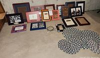 Photo showing various small photo frames and decorative items laid out on the floor, including black, maroon, blue, red, orange frames and round pressed flower hangings.