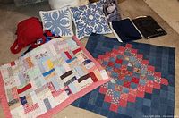 Two small patchwork quilts and decorative pillows with blue and white floral patterns. Dark blue towel bags and lace table cover visible on the side.