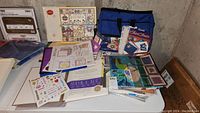 Scrapbooking supplies spread on table including albums, sticker sheets, paper packs, and a blue carrying bag