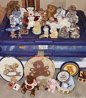 Full view of collection including small teddy bear stuffed animals, figurines, wall hangings, and tins displayed on blue storage boxes.