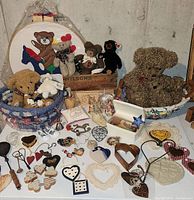 Full display showing rag baskets, teddy bears, small wall decor items including wooden and metal hearts, crocheted doilies, and assorted Americana ornaments on white table
