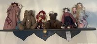 Photo showing nine vintage Americana decor pieces arranged on a dark wood wall shelf including rag dolls and teddy bears.