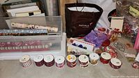 Photo of multiple rolls of wrapping paper stored in a plastic container, several spools of ribbon lined up in front, and a gift bag labeled Papyrus.