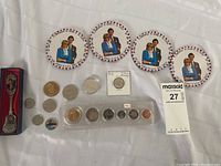 Photo showing four Princess Diana and Prince Charles coasters, a Bill Clinton souvenir spoon in a box, and multiple coins including a large silver coin in a coin flip labeled 1717.