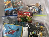 Multiple Lego sets and pieces in clear bags, including unopened Ninjago pack and instruction manual for red helicopter set.