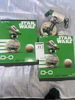 Front view of two Star Wars D-O interactive droids in original packaging, one sealed and one opened with the droid and accessories visible.