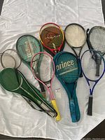 Lot of nine tennis and badminton rackets laid out on a white cloth, various colors and brands visible