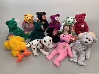 Photo showing 13 assorted vintage Ty Beanie Babies plush toys in varied shapes and colors, some standing and some sitting, all with heart tags.