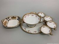 Overall view of serving bowl on saucer, six teacups, and ornate square platter/tray