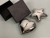 Two nickel-plated baby coin banks in heart and star shapes with original DANSK box.