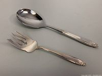 Two sterling silver handled serving utensils, a large serving spoon and a serving fork, shown side by side on a flat surface.