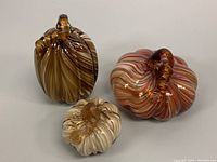 Three Murano style blown art glass pumpkin sculptures in amber, cream, and brown swirl colors displayed together.