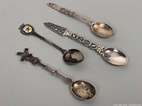 Three decorative silver spoons laid out showing fronts, highlight Egyptian themed spoon and detailed handles.